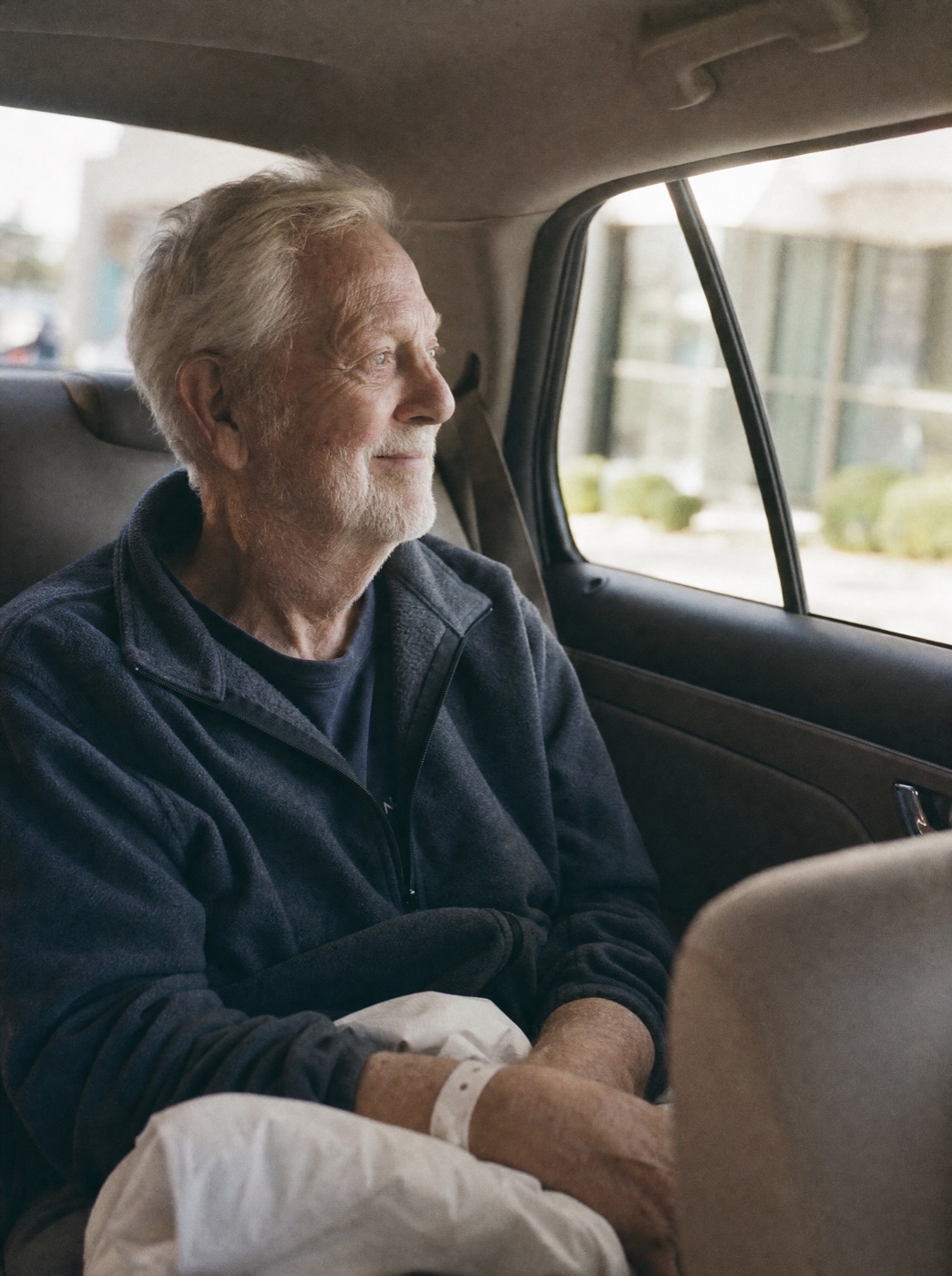 An older man riding home in the back of a car
